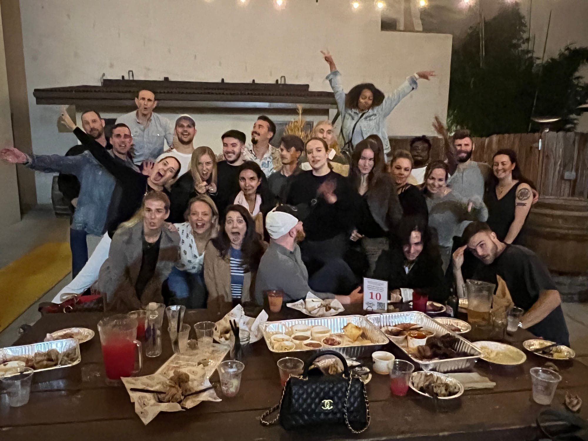About twenty-five people cheering around a long dinner table on a patio at night.