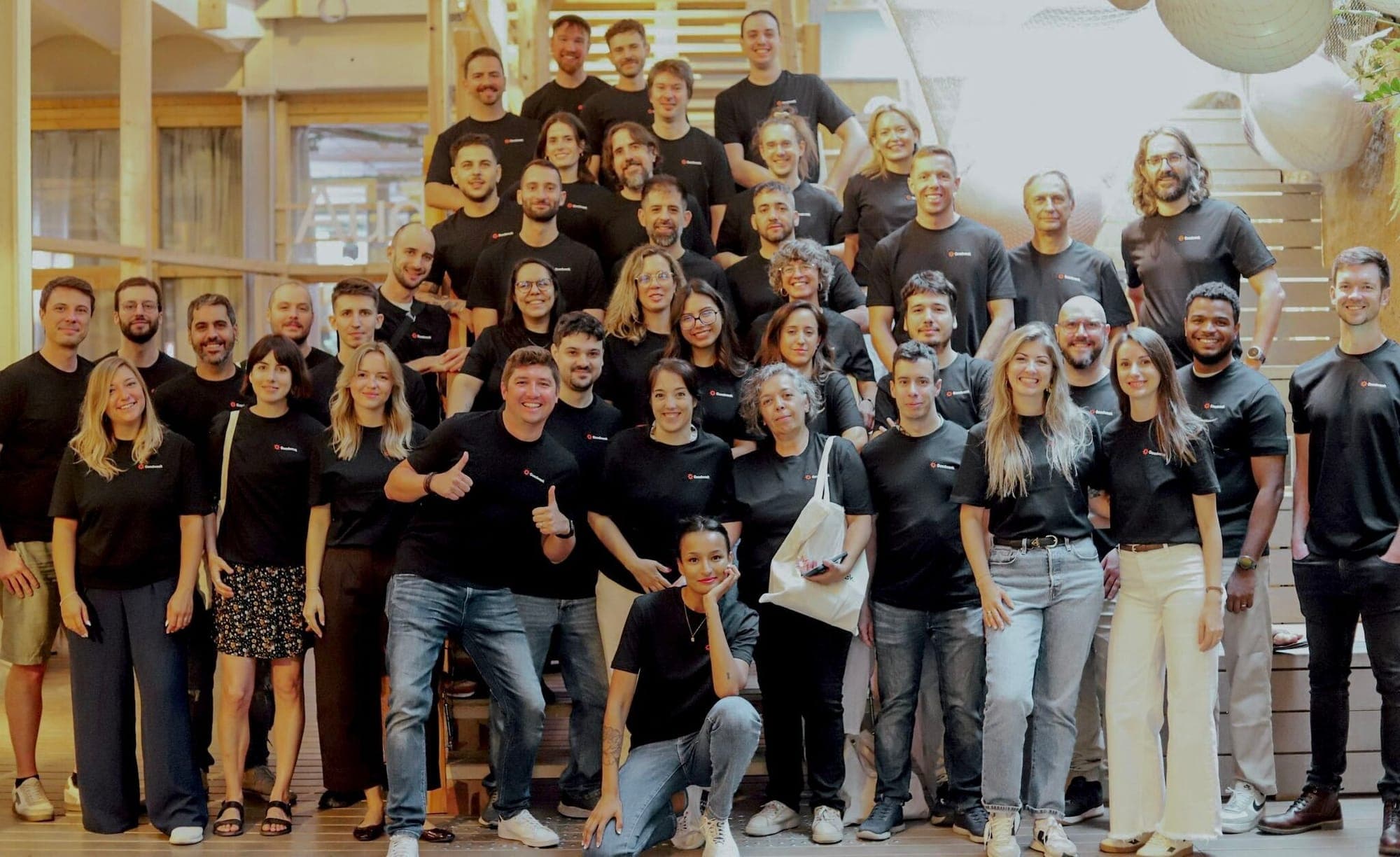 About fifty members of the Goodweek team in matching black T-shirts, standing on wooden steps.