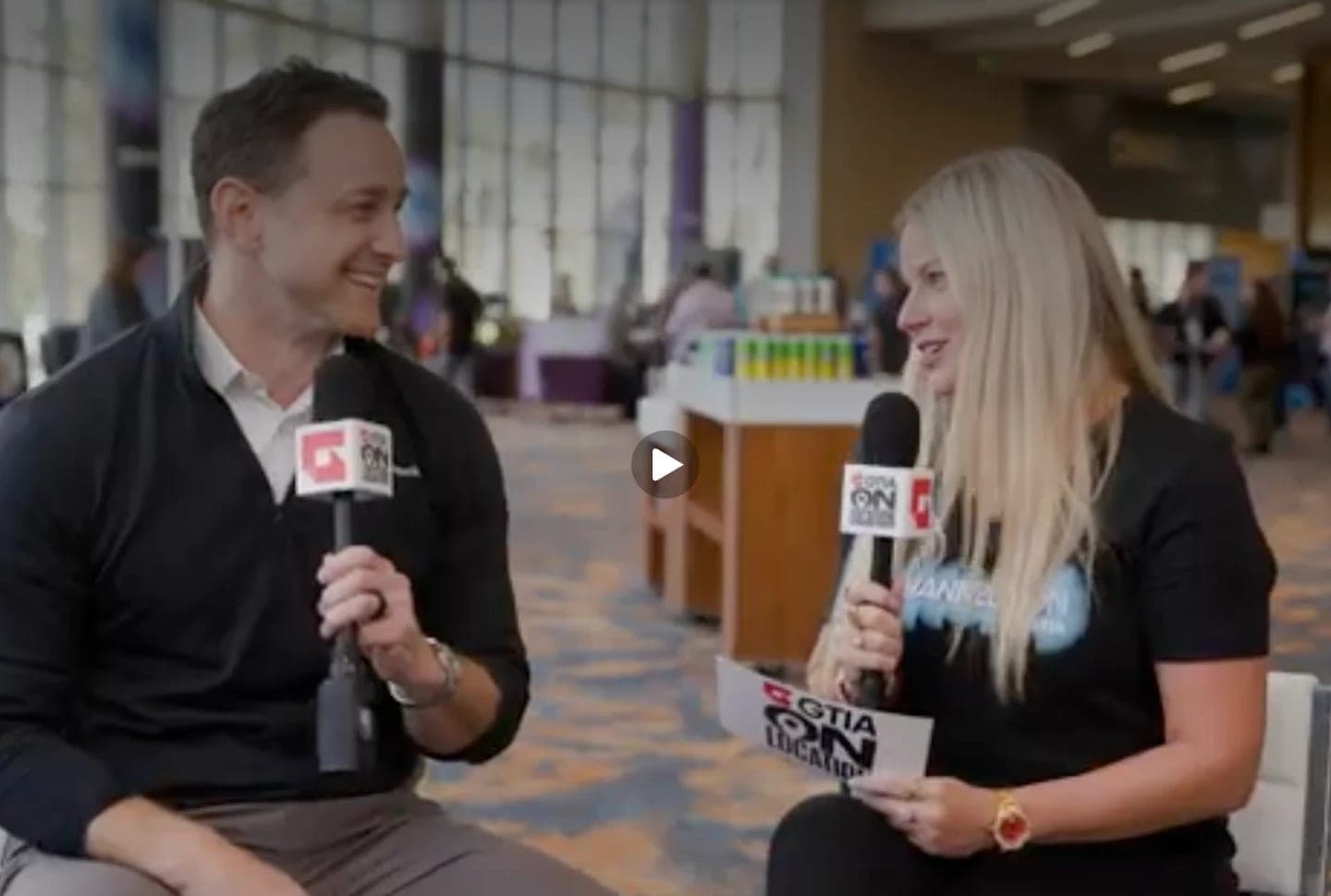 Mike and a GTIA On Location host seated with microphones in a conference hall, mid-interview.