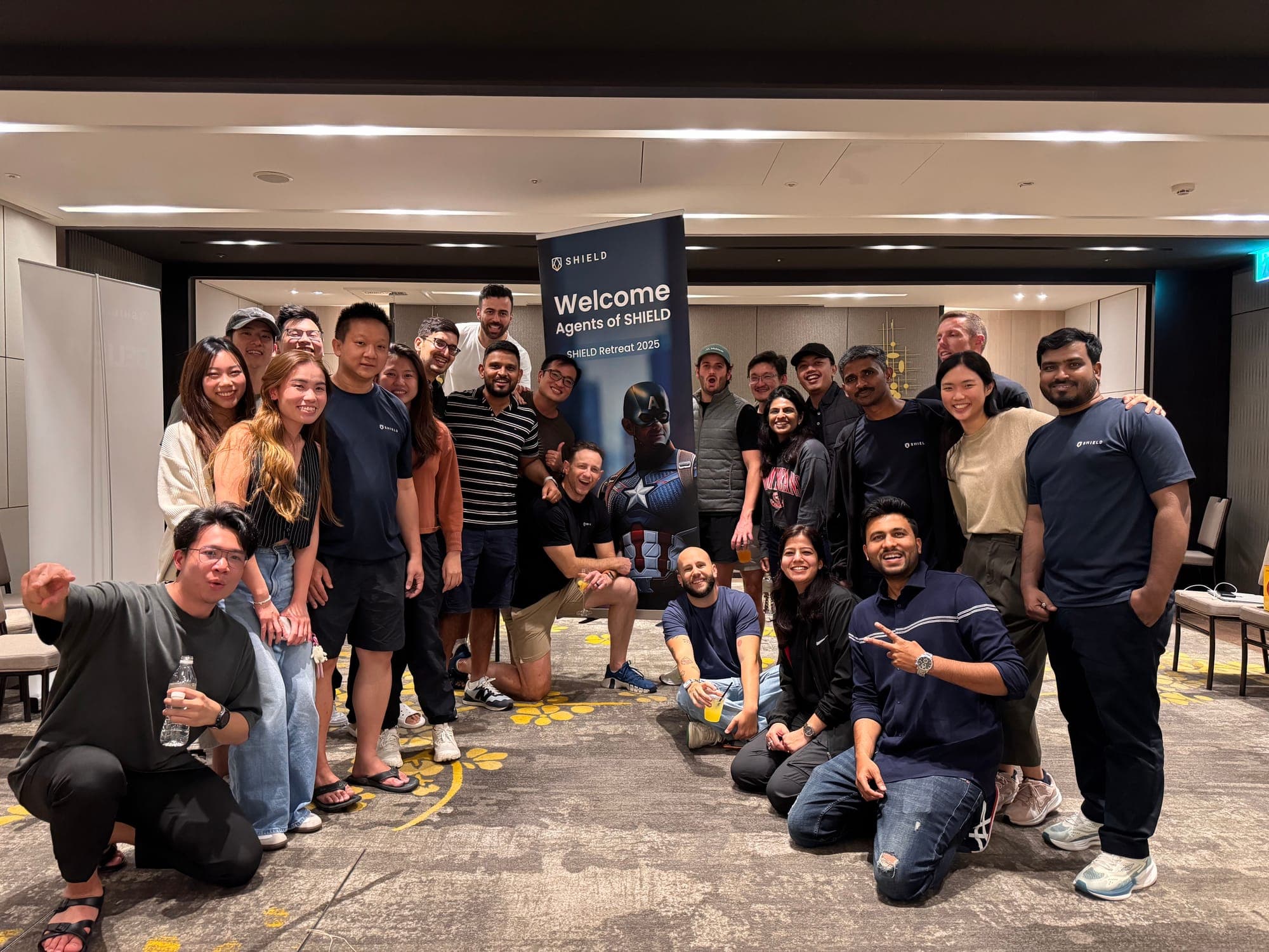 About thirty members of the SHIELD team posing around a banner that reads Welcome Agents of SHIELD, SHIELD Retreat 2025.
